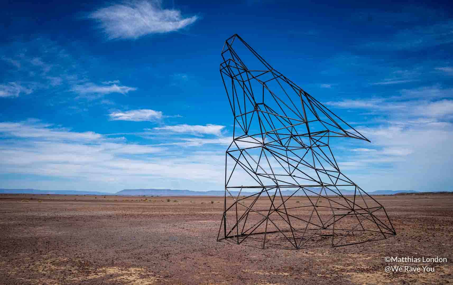 Return to the Source: Steel art installation of a wolf head in the desert.